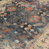 Detalle del patrón de la alfombra 'Alba', mostrando el diseño floral y geométrico en tonos de gris ahumado, beige, con acentos en rojo óxido y terracota. El efecto desgastado resalta el estilo bohemio