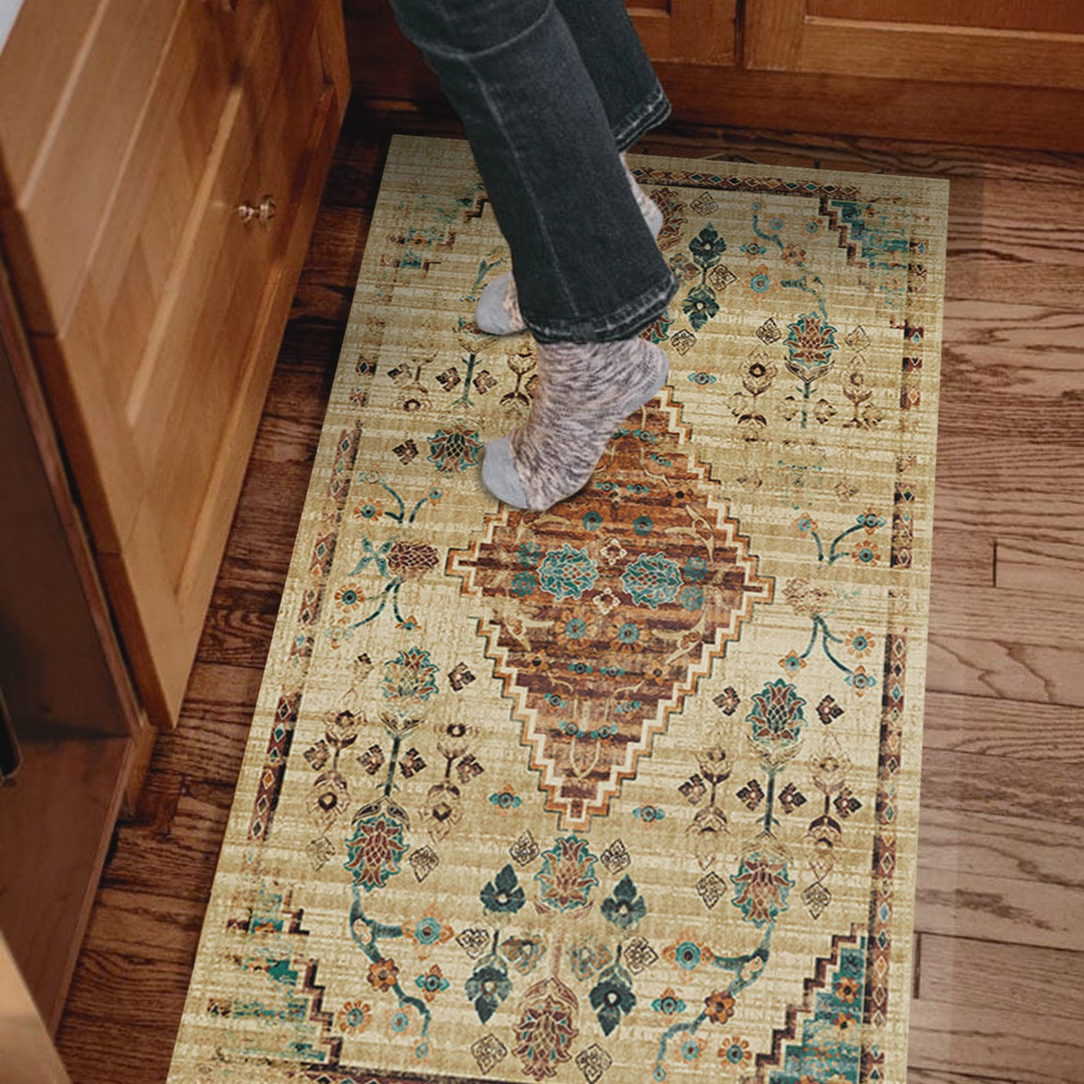 Alfombrilla 'Alegría' con el pie de una persona sobre ella, mostrando su diseño en tonos tierra, verde esmeralda y azul turquesa, y el fondo beige envejecido