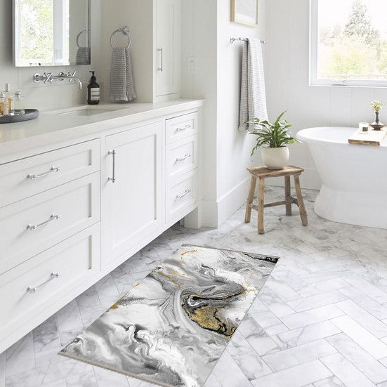 Alfombrilla 'Mármol' en un baño moderno y luminoso con gabinetes blancos, destacando su diseño en tonos de gris y blanco con toques dorados, aportando un toque de estilo al espacio