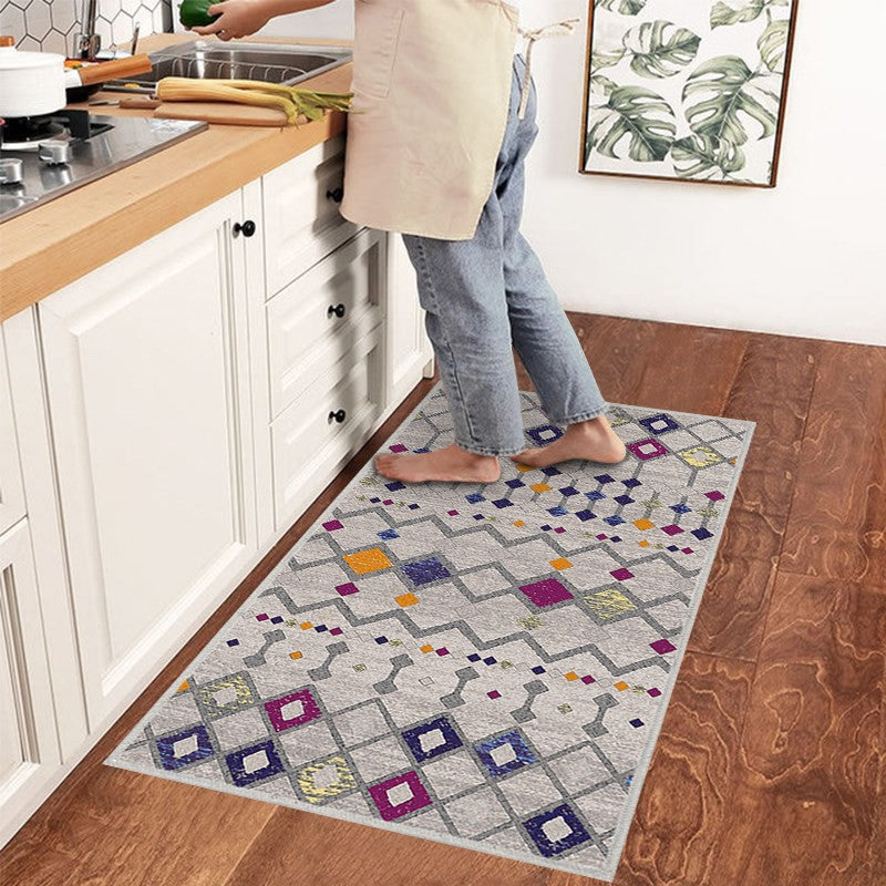 Alfombra 'Nadia' en una cocina, aportando un toque moderno y vibrante con su diseño en tonos púrpura, naranja, gris y blanco. Esta alfombra es lavable en lavadora, facilitando su cuidado en un entorno de alto tráfico.