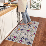 Alfombra 'Nadia' en una cocina, aportando un toque moderno y vibrante con su diseño en tonos púrpura, naranja, gris y blanco. Esta alfombra es lavable en lavadora, facilitando su cuidado en un entorno de alto tráfico.