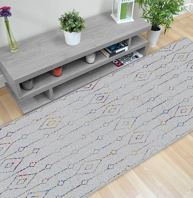 Alfombra 'Nora' en un salón moderno y luminoso, destacando su mezcla de colores vivos como azul, amarillo, rojo y púrpura sobre un fondo neutro. Añade elegancia y calidez al espacio, y es lavable en lavadora para una conveniencia adicional.