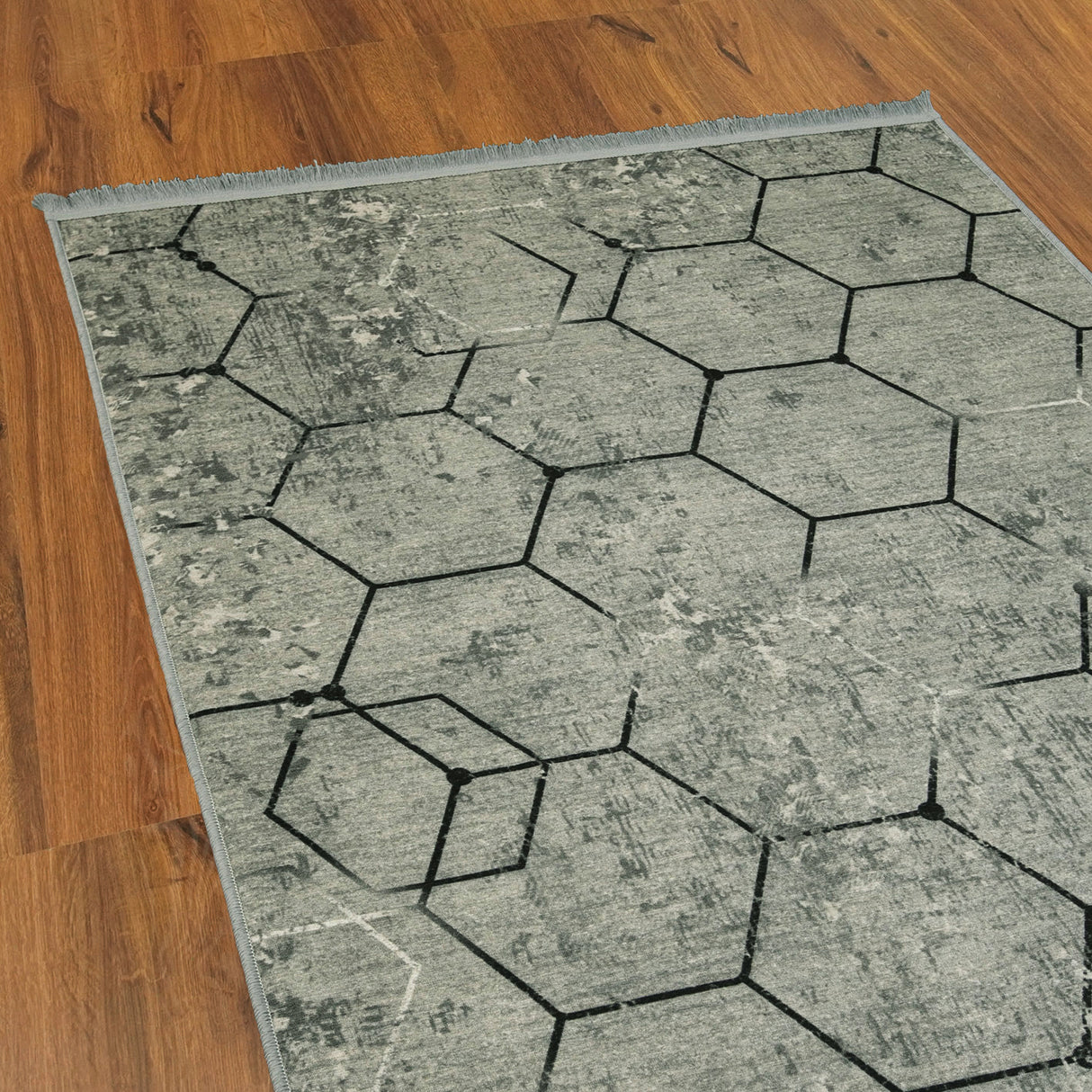 Esquina de la alfombra 'Terra', mostrando el patrón geométrico hexagonal en tonos grises que añade sofisticación y un toque moderno a la decoración.